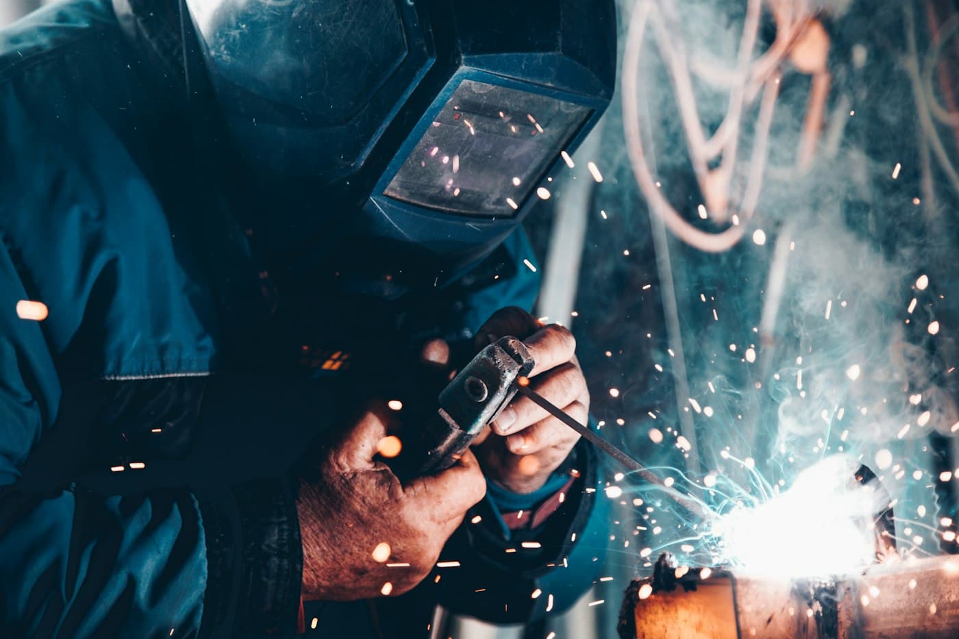 A welder in a helmet lays a bead as sparks fly